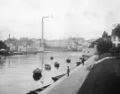 Refvens grund i Norrköping 1906. Då som ännu sökte man fiskelycka i Strömmens krök mot nuvarande Saltängsbron. I övrigt har miljön förändrats i grunden, men de något till åren komna Norrköpingsbor minns ännu Tuppens fabrikskomplex i fonden. Norrköpings Bomullsväfveri var dess egentliga namn, Tuppen i själva verket ett varumärke. Kallbadhuset var i någon mån mobilt och stod vid fototillfället förtöjt vid Strömmens västra sida. Träbyggnaden vid kajkanten till höger tjänade vid tiden som stadens klapphus.