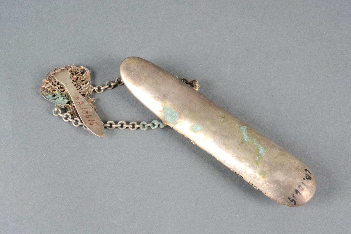 Brille- eller lorgnettfutteral av metall og fløyel. Til å henge i belte. Gjennombrutt rik ornamentikk anbrakt på fremsiden, glatt på baksiden. Foret med sort fløyel. Toppstykket har en hempe til å feste i belte eller skjørtelinning. To kjeder herfra holder selve futteralet.