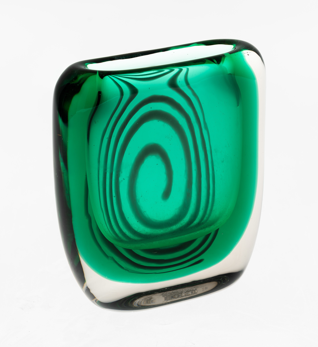 Tilnærmet kvadratisk vase med mykt buede sider i flerfarget glass. Toppen har en oval åpning på midten. Grønnfarget kjerne med blå spiral på en side, omgitt av klart overfang. Planslipt bunn.
