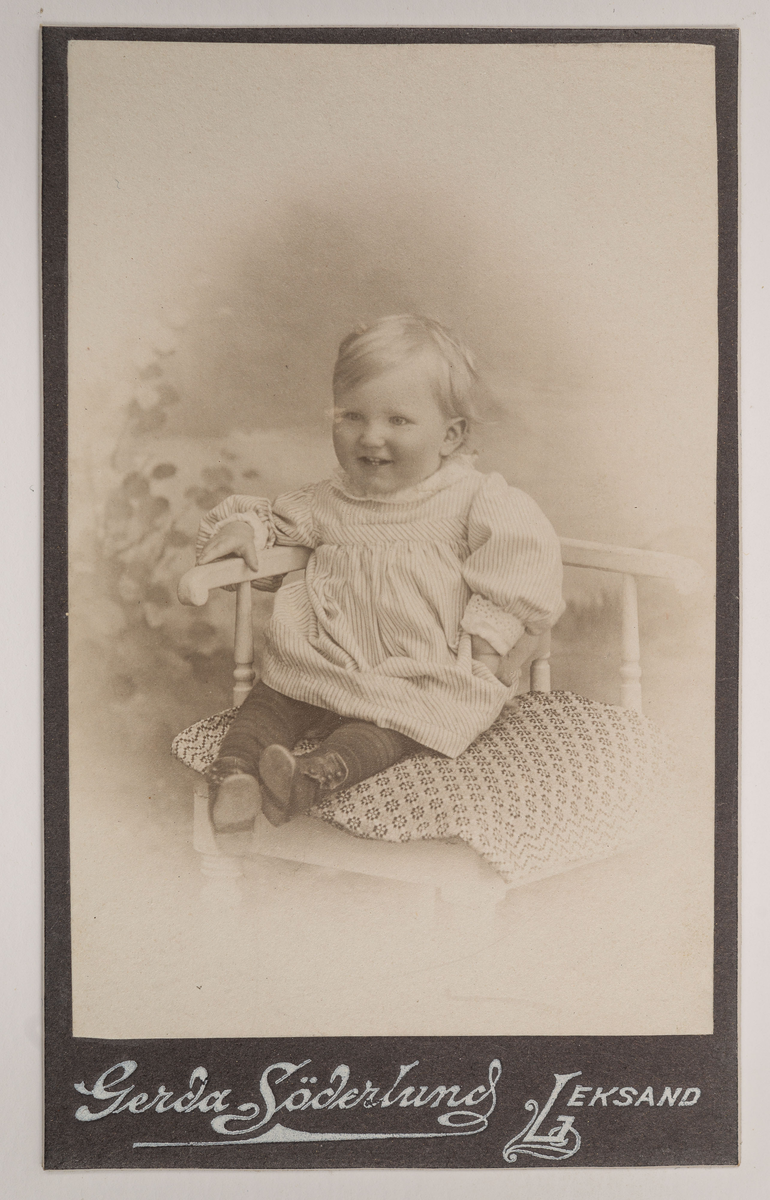 Visitkortsporträtt av Hilma Thorells och Landsfiskal Thorells barn, Åke Thorell. Fotografiet sitter i fotoalbum som tillhört Gertrud Zachau. Fotografiet sitter på sida 27.