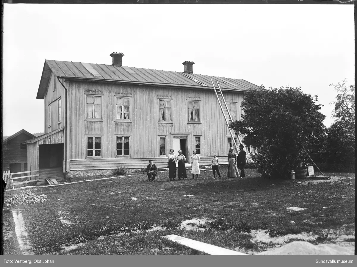 Två bilder från en gård. På första bilden pågår slåtter och hela familjen hjälper till. Två hästar är spända framför en slåttermaskin och en pojke håller ytterligare en häst. På andra bilden är människorna uppradade framför mangårdsbyggnaden som ser ut att vara spönad men inte målad.