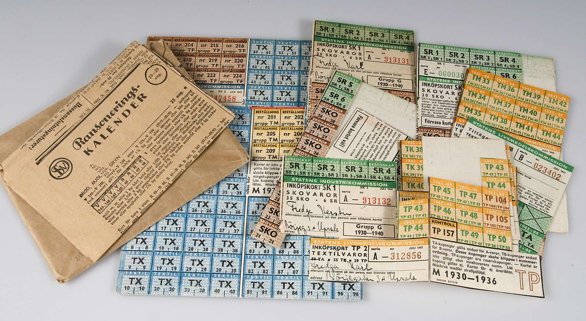 Brunt kuvert Ransoneringskort  för textil och skovaror utgivna av Statens Livsmedelskommission, utställda på olika medlemmar i familjen Fredga, Börjegatan 3 A, Uppsala: Arne, Brita, Karl, Björn, Sven, Märta , Kerstin Fredga. Samt ur tidningen utklippt Ransoneringskalender från 1944, gulnad.