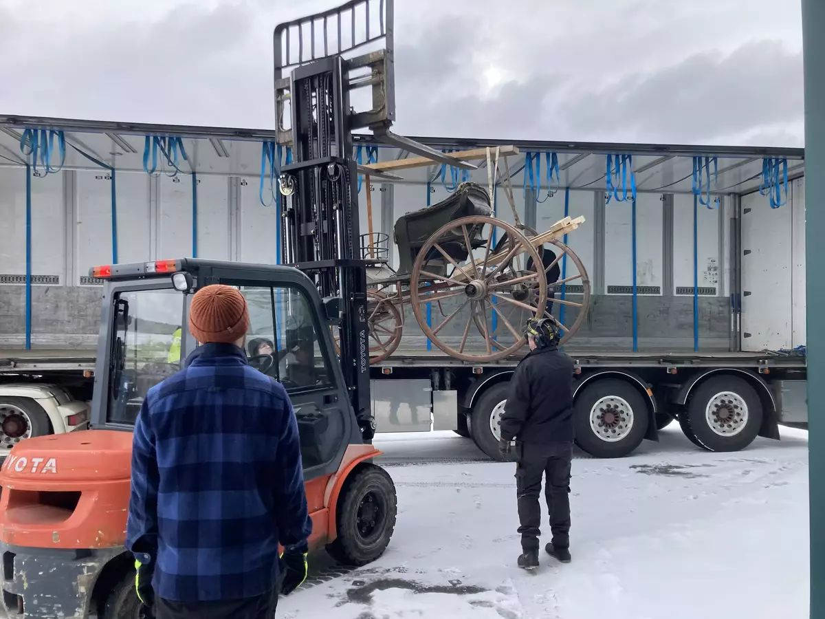 En gammel vogn lastes ombord en trailer med truck.