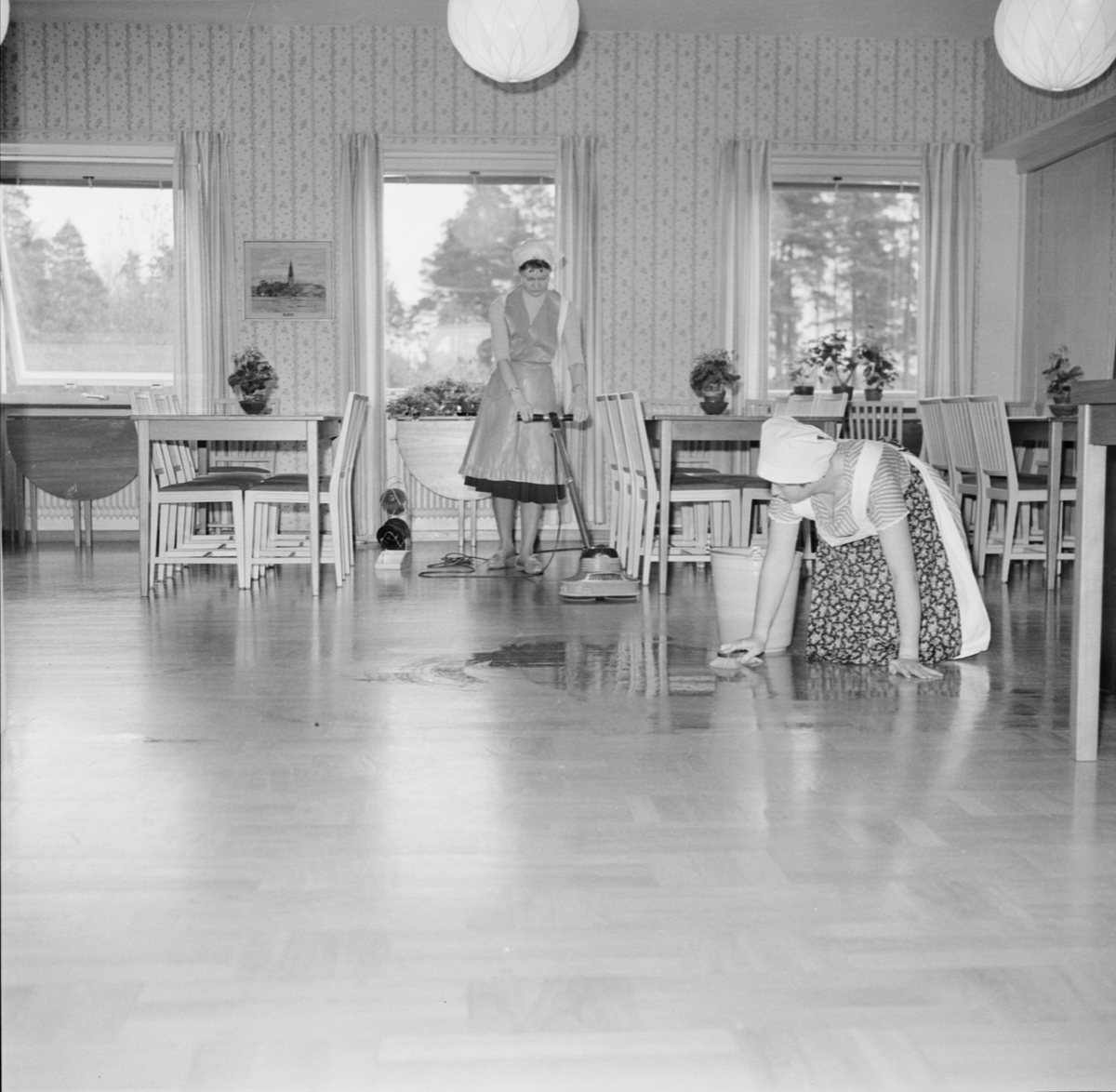 Parkettgolvet skrubbas rent med skurborste av Maj-Britt Thorslund, Liz Jansson bonar med maskin, sannolikt på Källgårdens Lanthushållsskola