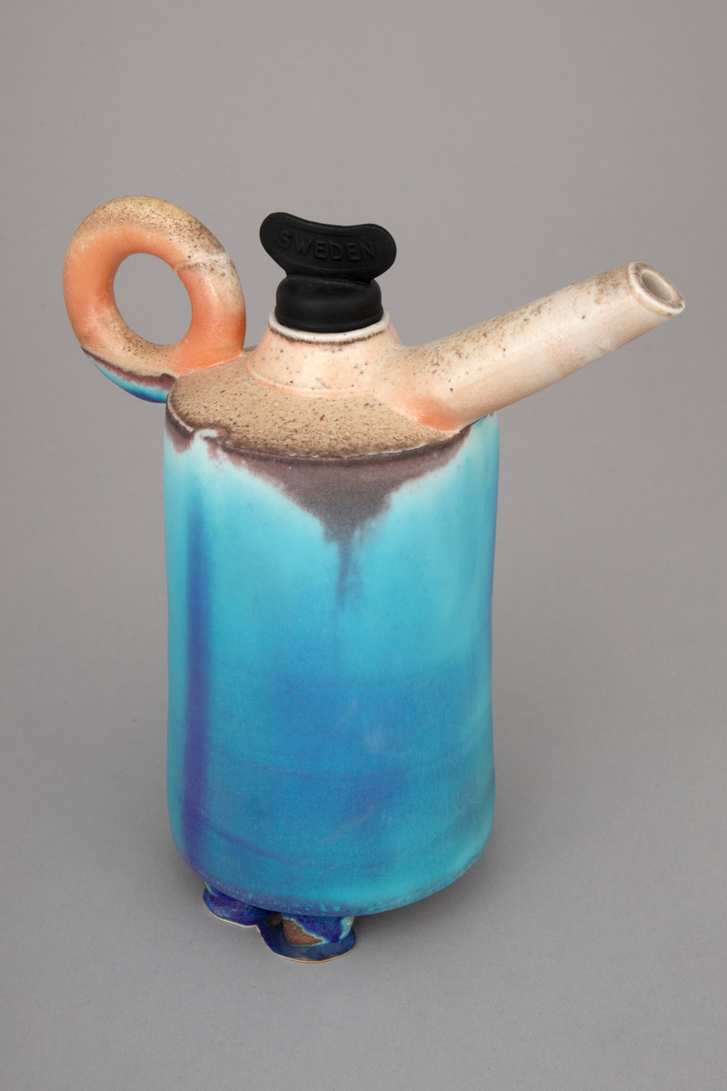 Installasjon med seks polykrome kanner i håndbygd porselen på et rustent bord med glassplate. Kannene er glasert og vedfyrt. Korkene på fem av kannene er lagd av funne komponenter. En har en korkopptrekker, to har industrielle komponenter i lakkert stål og to har gummikomponenter.