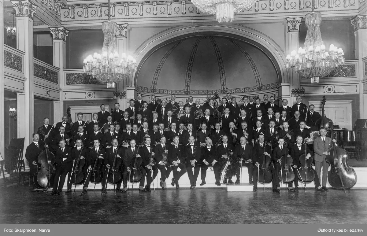 Fredrikstad Musikkforening og Oslo Handelstands orkester holdt to felles konserter i Fredrikstad (1927) og Oslo (1928). På bildet er de to orkestrene fotografert i den store sal i  Den Gamle Logen i Oslo.  Der holdt de konsert 11. mars 1928. 
Dirigenter var Severin Svendsen (nr. 10 i første rad fra venstre) og Gustav Lange (nr. 11 i første rad fra venstre).
Den andre konserten ble holdt  i Fredrikstad (biblioteket) 6. mars 1927. 
Personen til høyre for Lange holder en laubærkrans.
