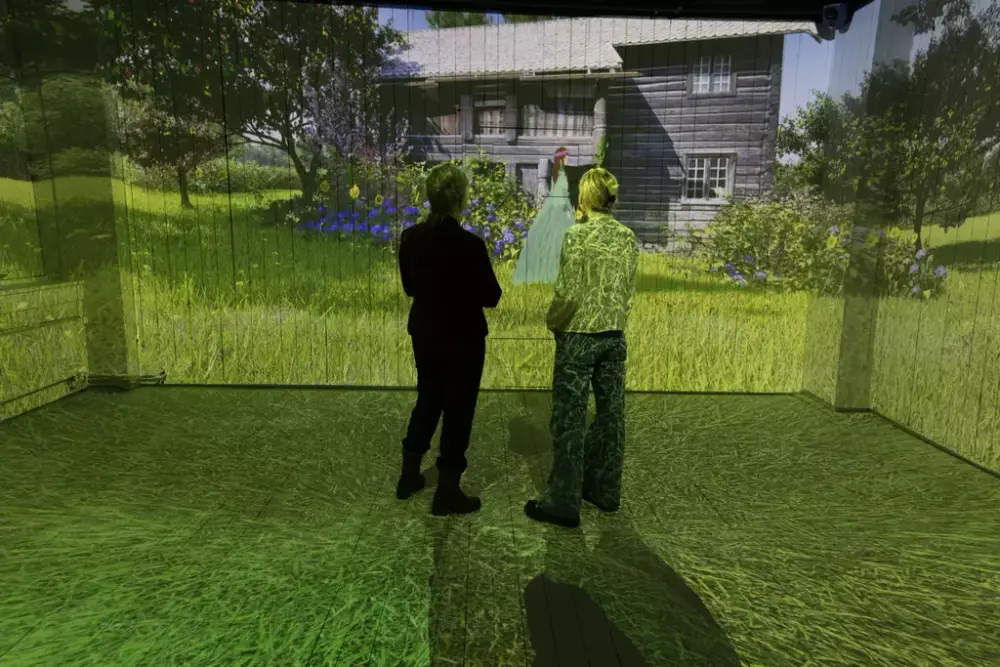 To kvinner står i et rom hvor en film om Ibsens verker utspiller seg på alle veggene. 