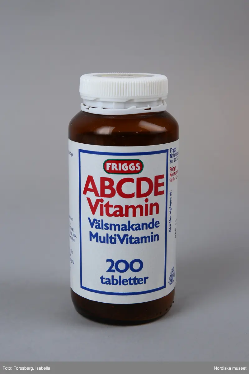 Huvudliggaren:
"Vitaminburk, glas, plast. Cylindrisk glasburk, brun, skuldra, vit skruvkork plast. Etikett vit, blå/rött tryck Friggs ABCDE vitamin. Tillv 1994 Friggs naturprodukter, Bromma. H 14 Diam 6 cm. Gåva 14/9 1994 av Åhlens City Stockholm."
