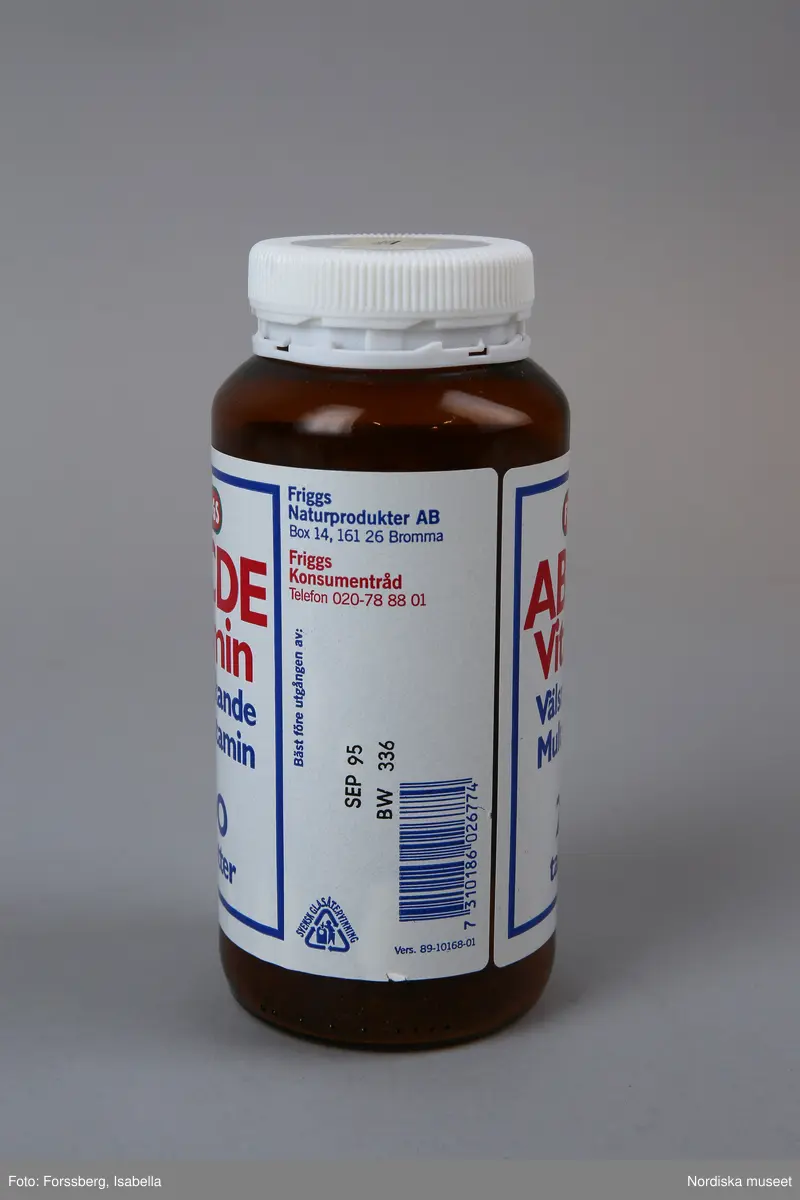 Huvudliggaren:
"Vitaminburk, glas, plast. Cylindrisk glasburk, brun, skuldra, vit skruvkork plast. Etikett vit, blå/rött tryck Friggs ABCDE vitamin. Tillv 1994 Friggs naturprodukter, Bromma. H 14 Diam 6 cm. Gåva 14/9 1994 av Åhlens City Stockholm."