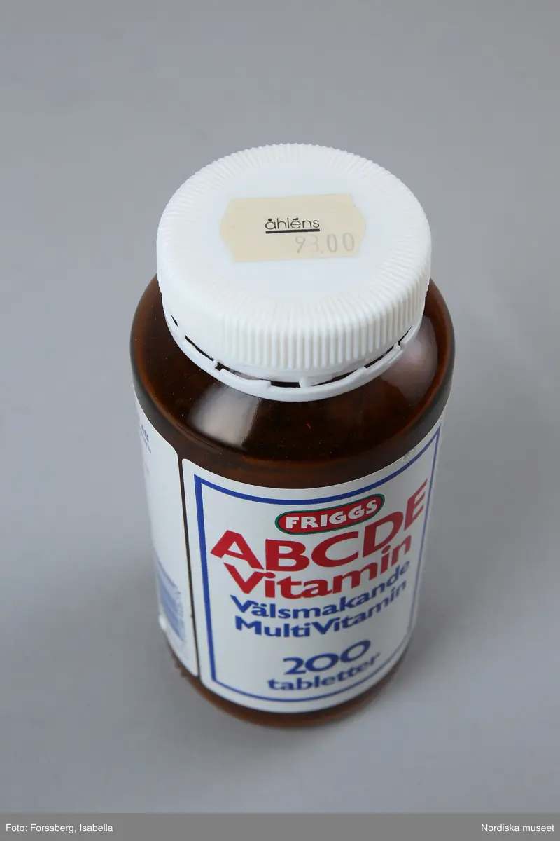 Huvudliggaren:
"Vitaminburk, glas, plast. Cylindrisk glasburk, brun, skuldra, vit skruvkork plast. Etikett vit, blå/rött tryck Friggs ABCDE vitamin. Tillv 1994 Friggs naturprodukter, Bromma. H 14 Diam 6 cm. Gåva 14/9 1994 av Åhlens City Stockholm."