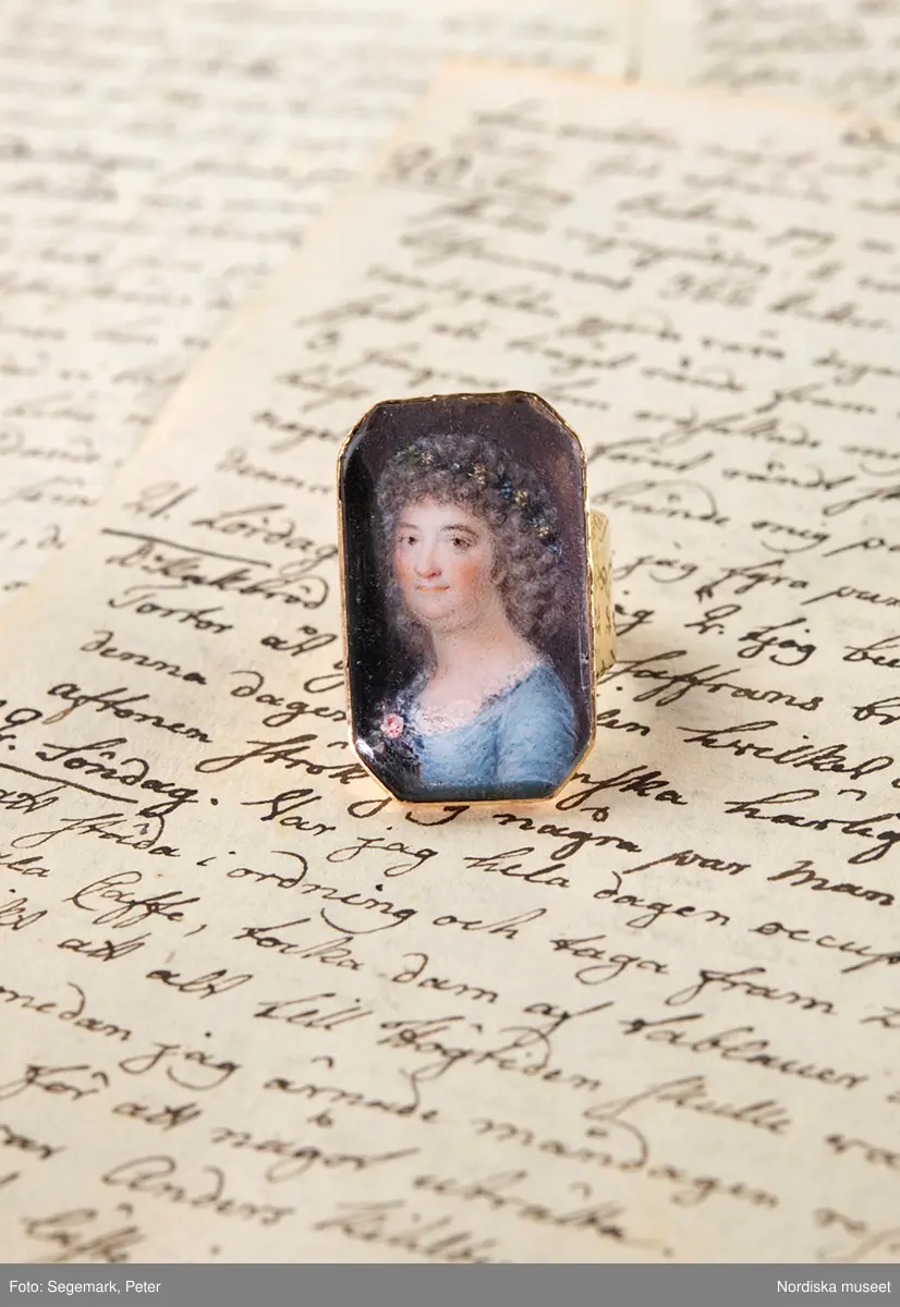  Ring av guld med miniatyrporträtt föreställande Märtha Helena Reenstierna. Målat 1796 på ben i gouacheteknik av Jacob Henric Rönngren (1756-1822) på beställning av M.H.R. även kallad "Årstafrun". Ringen avsedd som gåva till hennnes make ryttmästaren Christian Henric von Schnell på hans namnsdag den 13 november 1796. Graverat C.H.v.S. d. 13 Nov. 1796. 
Monteringen med 18K guld utförd av juveleraren Nils Hofsten. Stämplar: O2 (1796), S:t Erik, NH, 18K,  Kontrollmärke) Sannolikt omarbetad montering 1814.
Porträttet avbildar Märtha Helena Reenstierna i bröstbild sittandes i halvprofil iklädd blå klänning med liten rosenbukett i barmen. Hennes hår är friserat i täta små lockar, håret når nedaför nacken och hon har en smal rosengirlang runt håret. Ögonen bruna. Svagt rosa kinder. Bakgrunden mörk.

Jacob Henric Rönngren var kapten-mecanicus i arméns flotta. Han var född i Finland 1756 men slutade sina dagar i Stockholm 1822. Något dussin av hans miniatyrporträtt är kända - de flesta i Finland och vanligen knutna till officerskåren. Ett porträtt tillhör Finlands Nationalmuseum. I Nationalmuseum, Stockholm, finns sju miniatyrporträtt bl a av gmj Corfitz Beck-Friis (1724-1798), öljt David von Schewen (1770-1841) samt dåv kh i Finska församlingen, Bengt Lange.   

Nils Hofsten blev mästare som juvelerare i Stockholm 1788. Hans ritning till mästerstycke finns på Nationalmuseum. Hofsten stämplade 1795 -1805. Död 1814.
Ingrid Roos 2011-01-17
