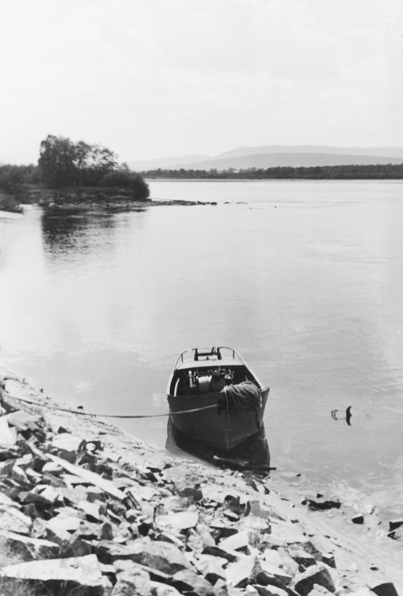 Liten varpebåt, fotografert fortøyd ved ei strand med et stilleflytende vannspeil i bakgrunnen. Dette er en åpen stålbåt med innvendig motor. Sentralt i den bakre delen av båten var det montert en kraftig vinsj med trekkvaier som gikk over en valse i akterenden av båten. I baugen lå det en taukveil. Dette fotografiet ble tatt i 1937, angivelig i Våler i Solør. Det var i dette tiåret Glomma fellesfløtingsforening tok i bruk denne båttypen, både i hovedvassdraget og et par av de større sideelvene, samt som supplement til de større slepebåtene på enkelte innsjøer. I boka «Fløting gjennom århundrer» (1998, s. 141) beskriver Øivind Vestheim bruken av denne båttypen slik: «Framgangsmåten var omtrent som ved bruk av spillflåte på sjø. Tømmer ble samlet i ringbommer som var festet til vaieren på båten. Varpebåten lot vaieren gå ut mens den kjørte framover til et feste på land eller i botn. Botnfester som besto av en festestokk som fløt i vannskorpa med en tung stein eller et betongkar som lodd, ble kalt «hengetjuver». Slike fester ble også brukt under varping med spillflåte. Varpebåten ble så gjort fast til festet, og tømmeret ble trukket mot båten ved å spille inn vaieren. Denne operasjonen ble for øvrig kalt «kraning» i Lomnessjøen i Rendalen. Varpebåtene kunne også trekke små tømmerbommer på slep slik som de store slepebåtene. Varpebåtene var også til stor nytte under landrensk i sjøer og sluttrensk i de større elvene.»