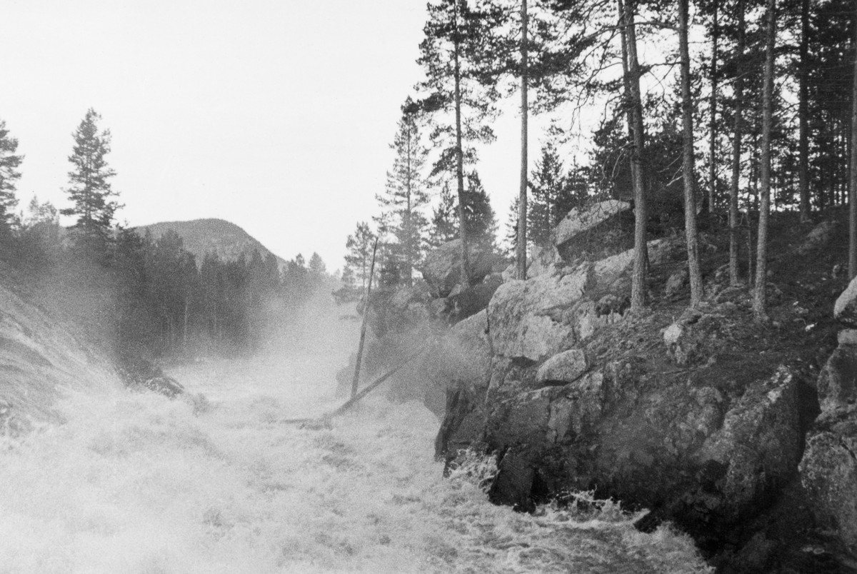 Fra Halkvernstupet, der Ytre Halåa forlater Halsjøen i Våler i Hedmark og renner gjennom ei 80-90 meter lang bergkløft med et fall på 9 meter. Fotografiet er tatt i andre halvdel av mai 1934, altså i en periode da det var rikelig med vann og betydelig fløtingsaktivitet i vassdraget. Bildet viser et kvitskummende strømkav der et par tømmerstokker reiste seg på høykant i den stride strømmen. Dette var en elvestrekning der tømmeret hadde hatt lett for å sette seg fast og bli påført skader. Forholdene var imidlertid noe forbedret etter at det var bygd skådammer langs den øvre delen av Halkvernstupet (jfr. SJF.1989-03069). I 1934 var det 73 795 tømmerstokker som ble levert ved Halåa og Halsjøen, og skulle gjennom dette vanskelige elvepartiet.