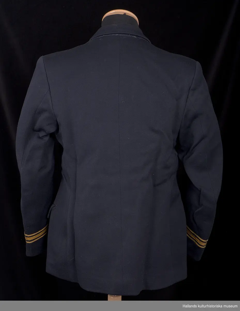 Kavaj till lotsuniform.

Dubbelknäppts uniformskavaj av marinblått tyg vävt i kypert. Bålen är fodrad med svart satintyg, ärmarna är fodrade med grått satintyg. Kavajen är i knäppningen försedd med 8 stycken runda gulmetallknappar präglade med emblem föreställande stockankare med tågvirke, krönt av en stjärna. På kavajens resp. krage ett emblem av gulmetall föreställande stockankare med tågvirke. På resp. armslut ett emblem av gulmetall föreställande en krona. Även tre band av förgylld tråd, varav det mellersta bandet är bredare än sidobanden.

Två fickor längs sidorna. Två invändiga fickor. Invändigt finns även hank för upphängning. Någon ägar- eller tillverkarmärkning upphittades ej vid inventering.