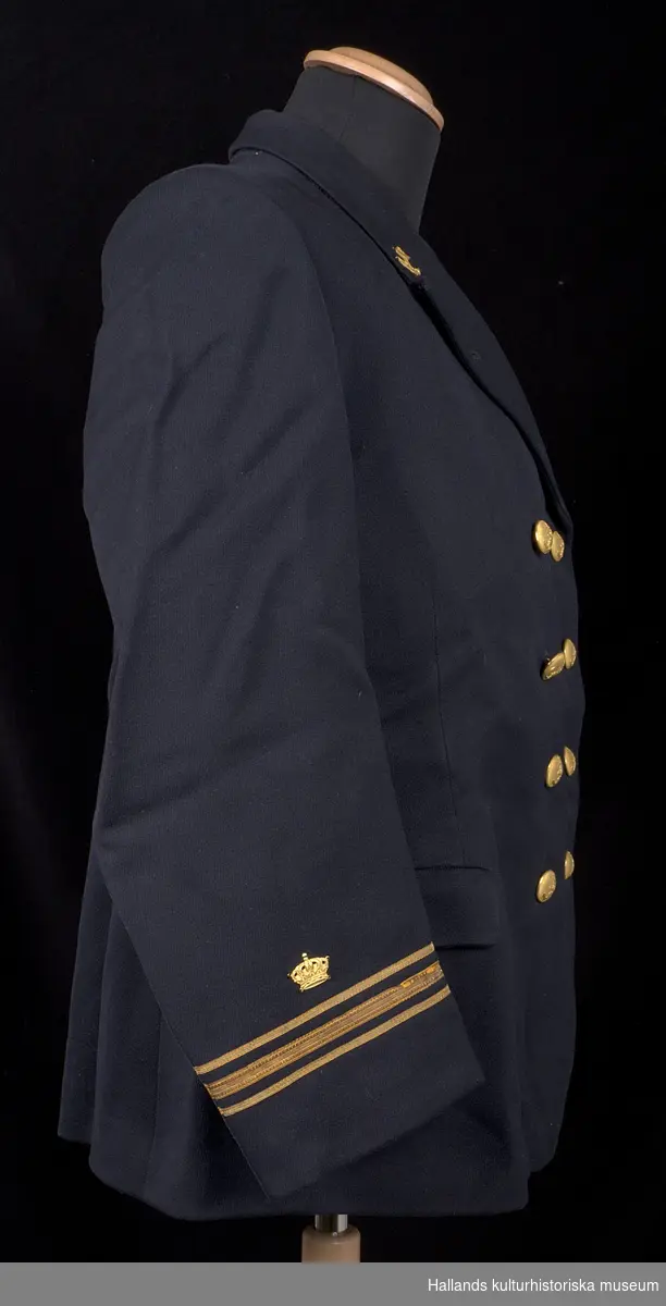 Kavaj till lotsuniform.

Dubbelknäppts uniformskavaj av marinblått tyg vävt i kypert. Bålen är fodrad med svart satintyg, ärmarna är fodrade med grått satintyg. Kavajen är i knäppningen försedd med 8 stycken runda gulmetallknappar präglade med emblem föreställande stockankare med tågvirke, krönt av en stjärna. På kavajens resp. krage ett emblem av gulmetall föreställande stockankare med tågvirke. På resp. armslut ett emblem av gulmetall föreställande en krona. Även tre band av förgylld tråd, varav det mellersta bandet är bredare än sidobanden.

Två fickor längs sidorna. Två invändiga fickor. Invändigt finns även hank för upphängning. Någon ägar- eller tillverkarmärkning upphittades ej vid inventering.