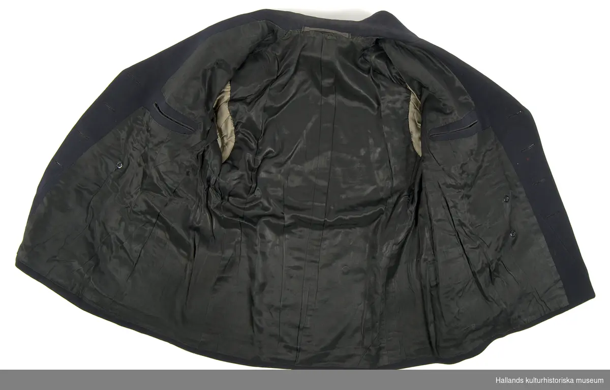 Kavaj till lotsuniform.

Dubbelknäppts uniformskavaj av marinblått tyg vävt i kypert. Bålen är fodrad med svart satintyg, ärmarna är fodrade med grått satintyg. Kavajen är i knäppningen försedd med 8 stycken runda gulmetallknappar präglade med emblem föreställande stockankare med tågvirke, krönt av en stjärna. På kavajens resp. krage ett emblem av gulmetall föreställande stockankare med tågvirke. På resp. armslut ett emblem av gulmetall föreställande en krona. Även tre band av förgylld tråd, varav det mellersta bandet är bredare än sidobanden.

Två fickor längs sidorna. Två invändiga fickor. Invändigt finns även hank för upphängning. Någon ägar- eller tillverkarmärkning upphittades ej vid inventering.