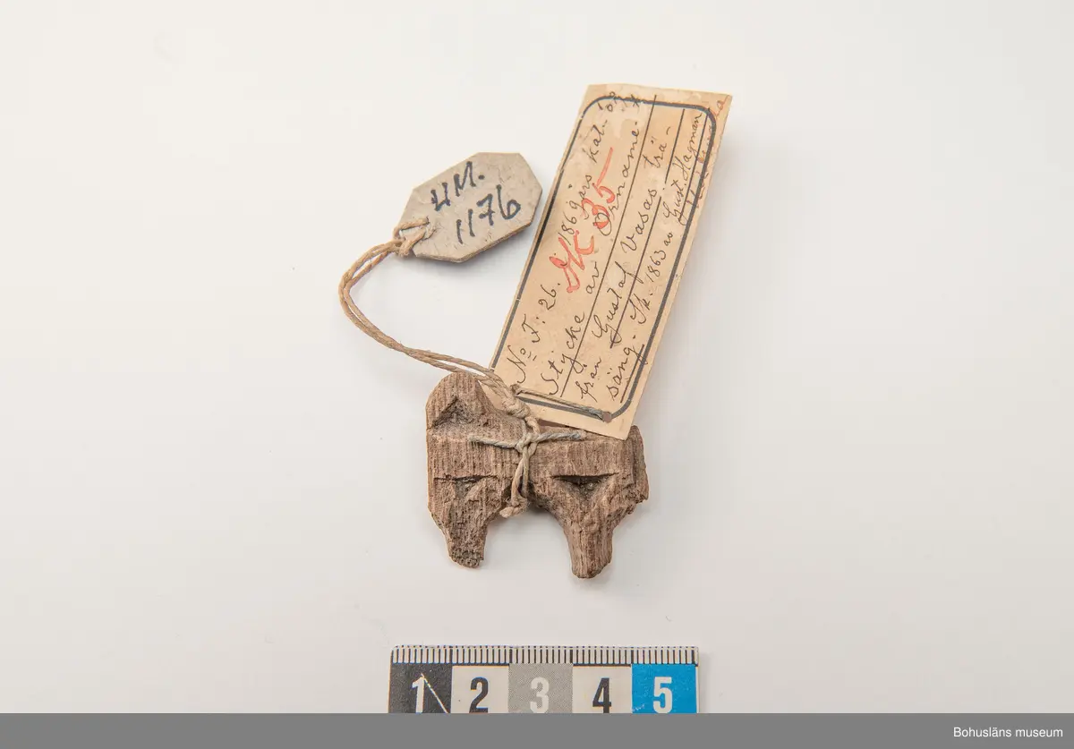 Fragment av större träföremål i ek, ornamenterad på framsidan i plattskärningsteknik. 
Enligt påskrift på äldre, vidhängande föremålsetikett: "Stycke av Ornament från Gustaf Vasas träsäng."
Ur handskriven katalog över Uddevalla Musei Historiska Samlingar, svenska avdelningen, yngre föremål upprättad  år 1916 av Knut Adrian Andersson, intendent från 1 oktober 1915:
"No 56 = (F:26 i 1869 års katalog av G. Brusewitz)
Stycke av trä-ornament från
Gustaf Wasas säng. Skänkt 1863 av Gustaf
Hagman i Uddevalla".

Ur handskrivna katalogen 1957-1958:
Stycke av träornamenet
Mått: 3,7 x 3,4 x 0,7 cm; (skall vara fr. Gustav Vasas säng).

Litt.: Utställningskatalog "Ärva och Förvärva Vårda eller Fördärva?", Stiftelsen Läckö institutet, 1995.
Utställningskatalog "Guide till svenska folkets kungaminnen", Livrustkammaren 2003.