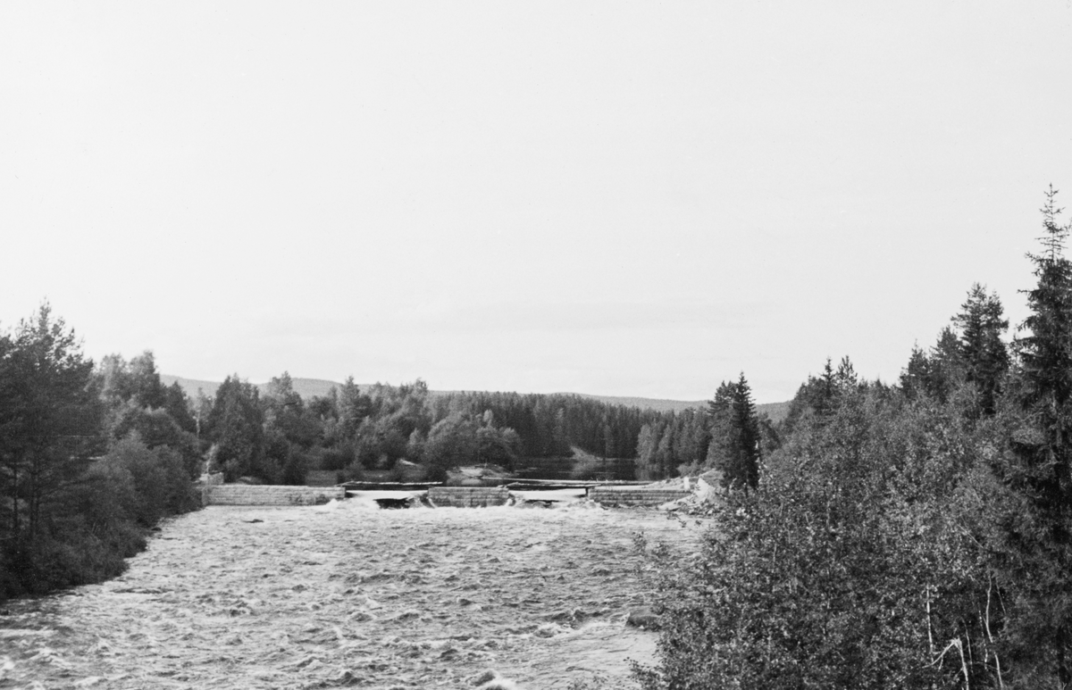 Dammen i Kjellåsfossen i elva Flisa i Åsnes kommune i Solør, fotografert i morstrøms retning høsten 1934. På dette tidspunktet, lenge etter at fløtingssesongen var over, sto dammen åpen. Det var imidlertid mye vann i vassdraget, antakelig fordi at bildet er tatt etter en kraftig regnværsperiode. Dammen hadde to elleve meter brede tømmerløp med mellomliggende kar som var murt av kvadrete steinblokker. Fløtingsteknisk sett var hovedpoenget med Kjellåsdammen og samle vann som kunne brukes til å få tømmeret til å flyte gjennom den nedenforliggende den av Flisa, også i perioder da den naturlige vannføringa var liten. Magasinkapasiteten var imidlertid beskjeden. Den dammen vi ser på dette fotografiet ble bygd i 1924, som en erstatning for en eldre Kjellåsdam.