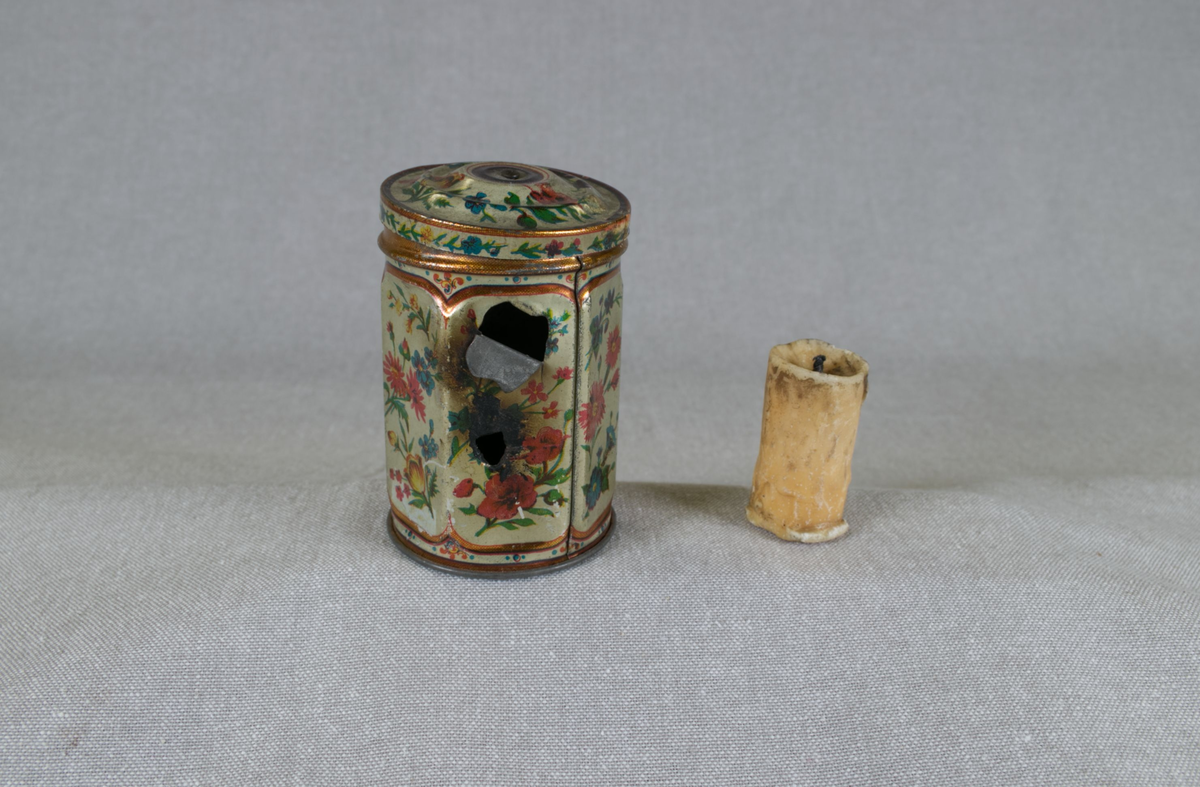 Montasje med 5 foto av Elias Tønnesen på en plate. Platen med bilder og tekst har nederst en påfestet plate for utstilling av "lykten", som er en sekskantet teboks, dekorert med blomster, og med to små hull for lyset. Teboksen inneholder en talglysstump.