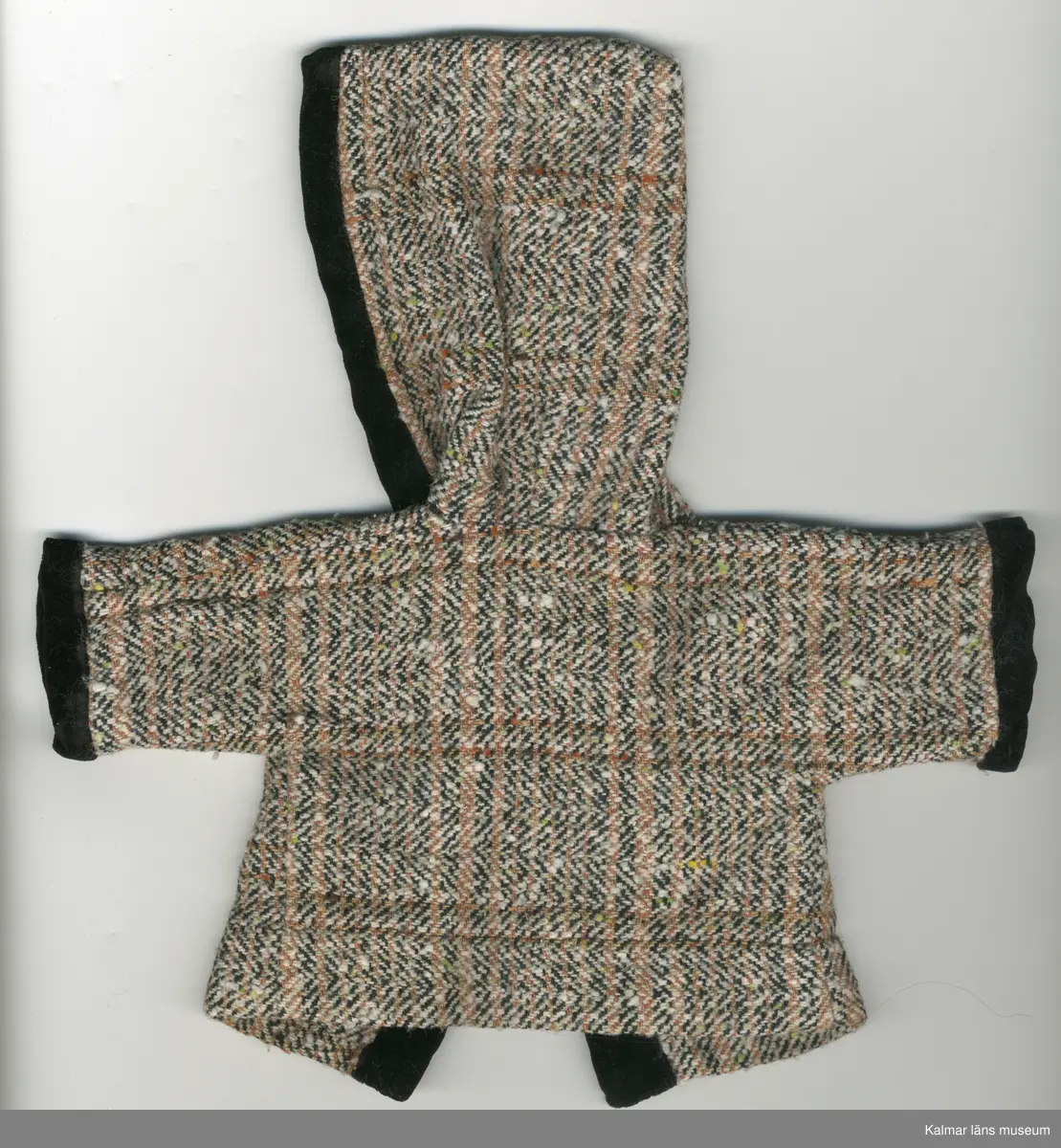 KLM 45519:16:10. Dockkappa, med huva, av konstmaterial, brun, vit och svartmelerad. Kappa kantad, framtill, även huva och ärm, nertill, med sammetskant, svart. Under huva, inuti kappa, bomullsband, rött, fastsytt med lösa ändar, som knyts