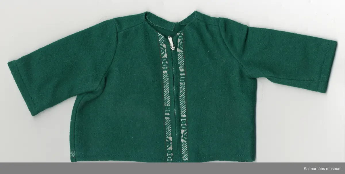 KLM 45519:17:10: 1-3. Dockdräkt, 3 plagg av textil, ylle, grönt. Mönsterbård, invävd, vit och grön med text: ALL WOOL. :1 Dockjacka, rundad halsurringning. dragkedja, framtill, vit. Mönsterbård, två stycken, framtill, längs dragkedja och en bak på jacka, nere vid fållen. :2 Dockbyxa, "sparkbyxa", byxa, hopsydd med rundning vid tår, vänster ben längre. Midja, linning med mönsterbård, knäpps i midja med hake och hyska, av metall. :3 Dockhuvudbonad, skärmmössa, av grönt ylle. Kulle och kant invändigt, förstärkt med Vlieseline, vitt. Mössa, kant, dekorerad med mönsterbård.