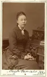 Studioportrett av kvinne sittende på stol.