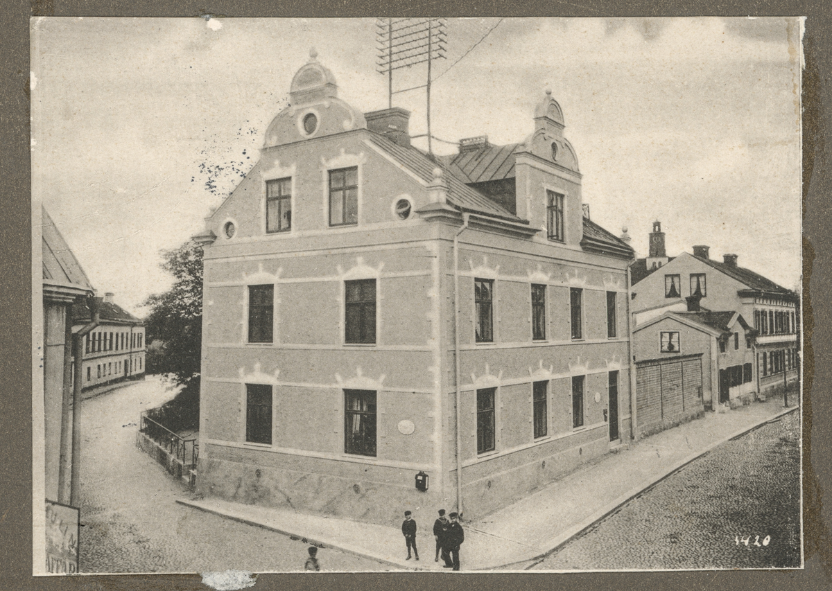 Ett beskuret vykort som är inklistrat på pärmens insida i vykortsalbum nr. EM06774:h. Vykortets motiv är Telegrafhuset i kvarteret Kaplanen, i korsningen Kungsgatan-Rådhusgatan, Enköping.