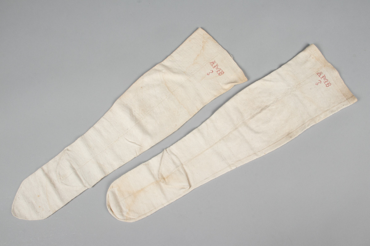 Et par hvite halvstrømper eller knestrømper i glattstrikket bomull med monogrammet AMB brodert i korsting øverst på hver strømpe