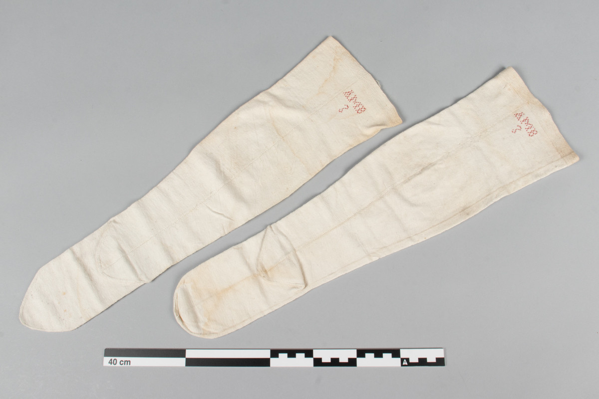 Et par hvite halvstrømper eller knestrømper i glattstrikket bomull med monogrammet AMB brodert i korsting øverst på hver strømpe