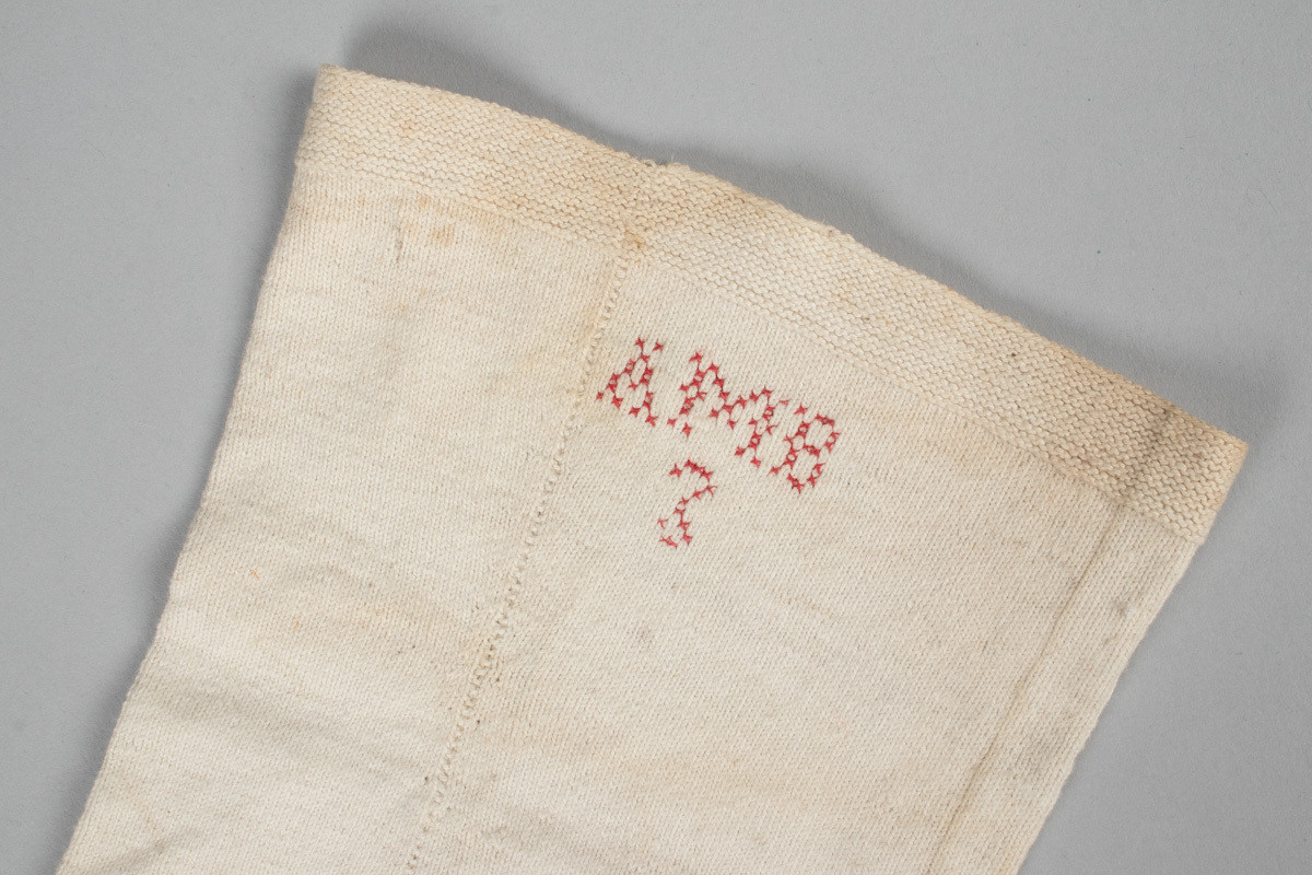 Et par hvite halvstrømper eller knestrømper i glattstrikket bomull med monogrammet AMB brodert i korsting øverst på hver strømpe