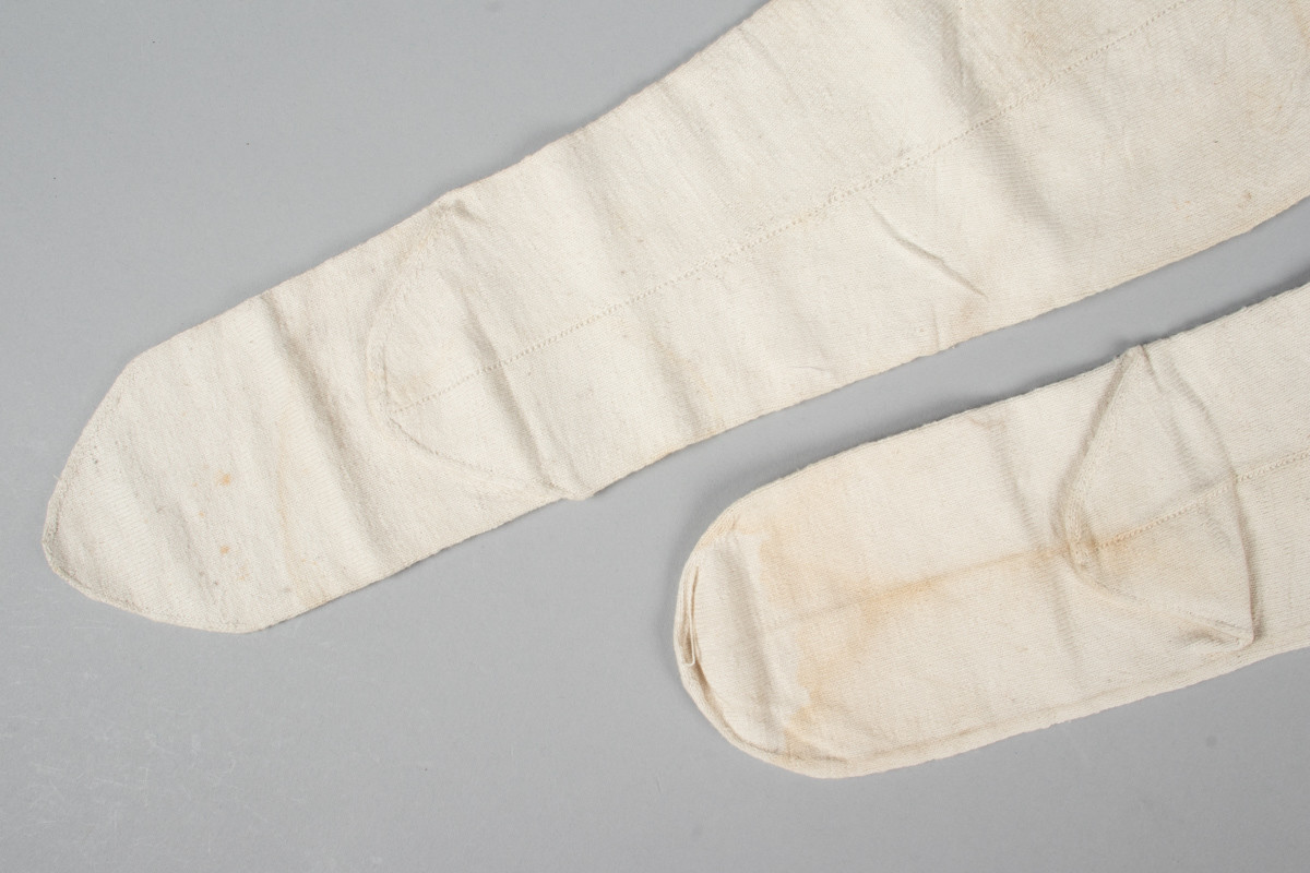 Et par hvite halvstrømper eller knestrømper i glattstrikket bomull med monogrammet AMB brodert i korsting øverst på hver strømpe
