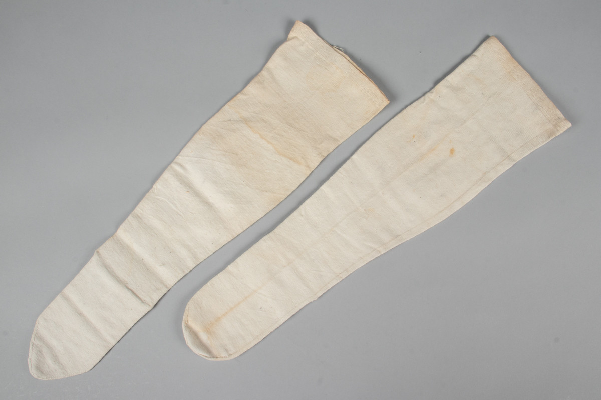 Et par hvite halvstrømper eller knestrømper i glattstrikket bomull med monogrammet AMB brodert i korsting øverst på hver strømpe
