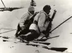 Två man med snödräkt och pälsmössa ligger och kikar över snövall med varsin kulsprutegevär m/1921.