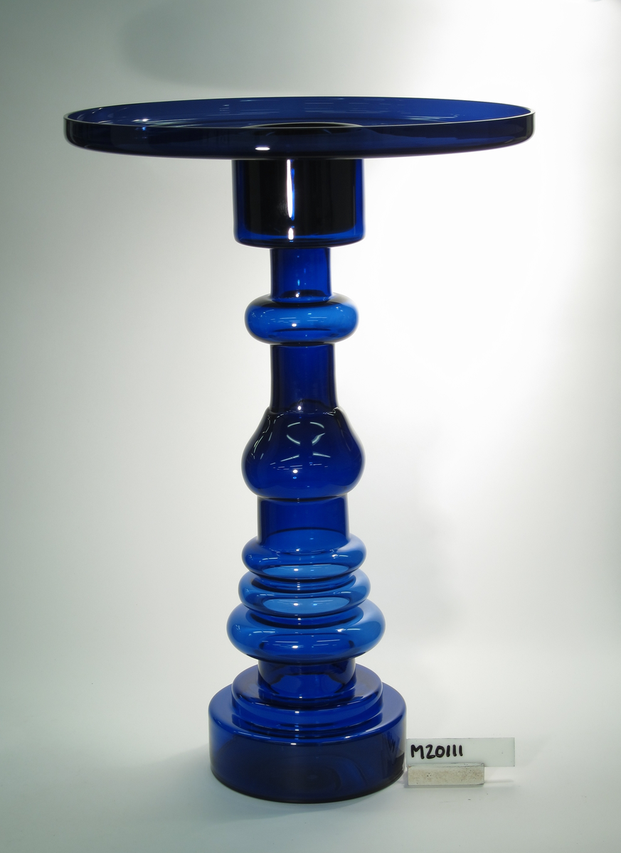 "Fyren" formgiven av Oiva Toikka. Blått glas. Övre delen ett löst insatt fat. Nedre delen en hög pelare med olikformade vulster.