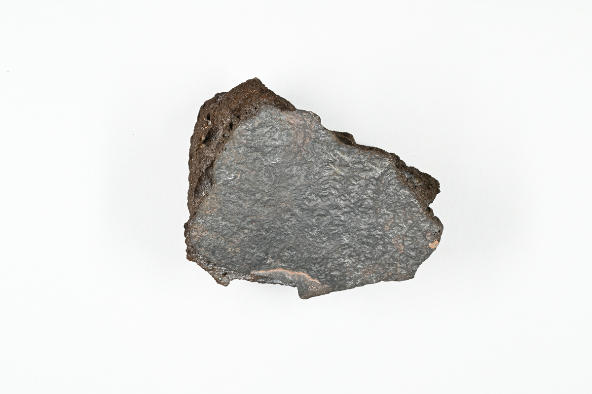 Slaggprov, svart med inslag av koppar. Tillhörande lapp med notering: "Slagg från råkoppar smältning i Kafveltorp, 1902, J. Petrén.".