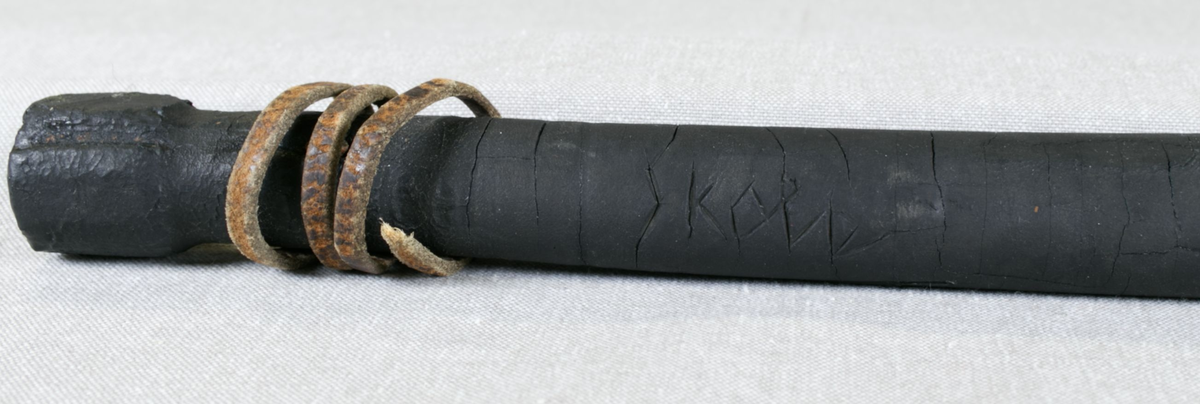 Sort gummikølle med bly i tuppen og lærsnor. Innskåret "M" i enden og "Skola" på siden.