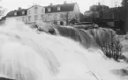 Tinnebäckens flöde utmed området Sandbäcken i Linköping. Det var ingen slump att fotografen sökte sig till ett av bäckens större fall just våren 1924. Året bjöd på ett särdeles kraftigt vårflöde som i hela landet hamnade på vykort. Av lokalhistoriskt värde fick vi i detta fall även en god återgivning av den sällan avbildade huvudgården till fastigheten Sandbäcken. Den långa huslängan uppfördes ursprungligen omkring 1810 som bostad för bruksarbetare vid ett då nyanlagt tegelbruk på platsen. Huset kom över tid att om- och tillbyggas för att slutligen rivas 1958.