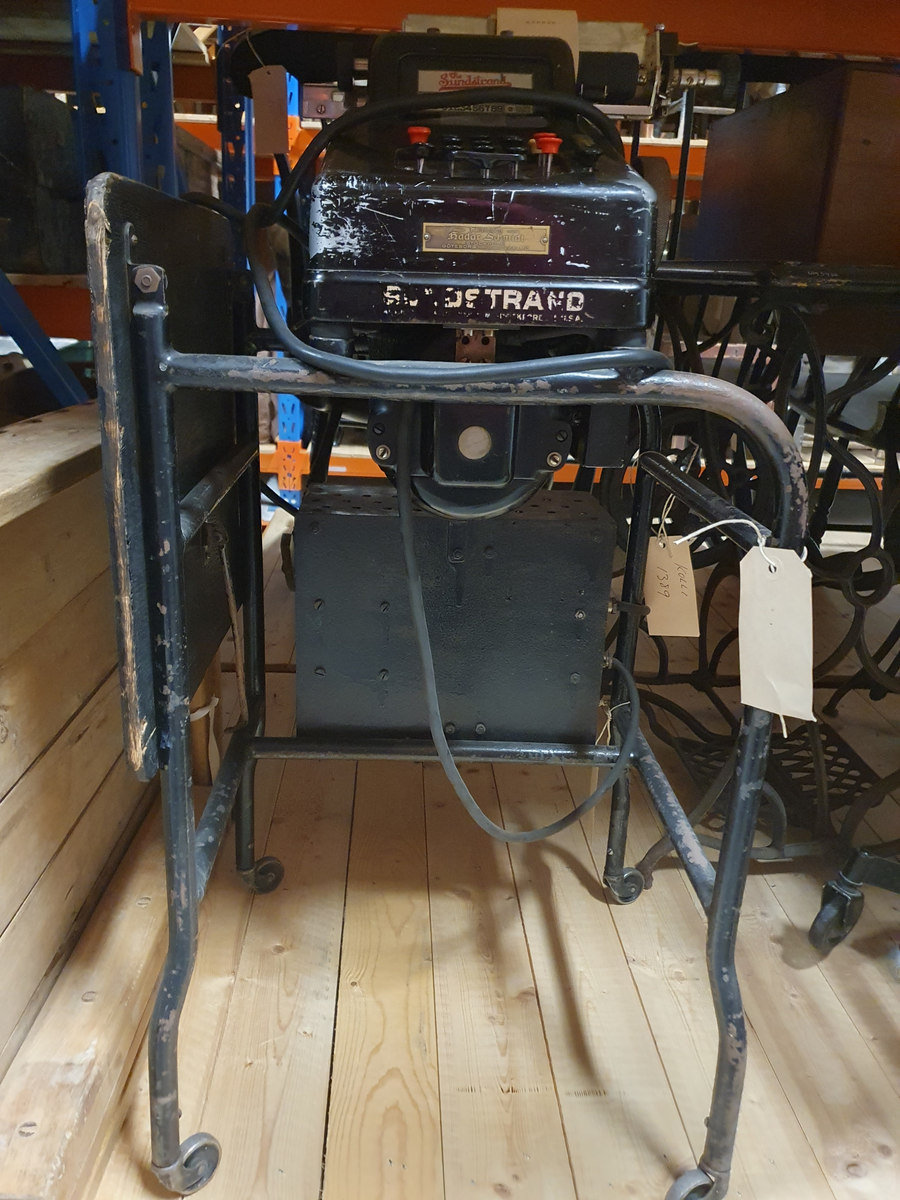 Räknemaskin på rullbord. Elektrisk motor och elsladd. Svartmålad plåt. Bordsbricka på bordet, kan fällas. Räknemaskinen är 20 cm bred, 15 cm hög, 37 cm djup. Handdriven vals med isatt pappersrulle. Knappsats med röda och svarta knappar. Etikett "The Sundstrand" REG´D TRADE MARK TEN, THOU, MILL, COLUMNS LISTING 0123456789, 9 column totals.