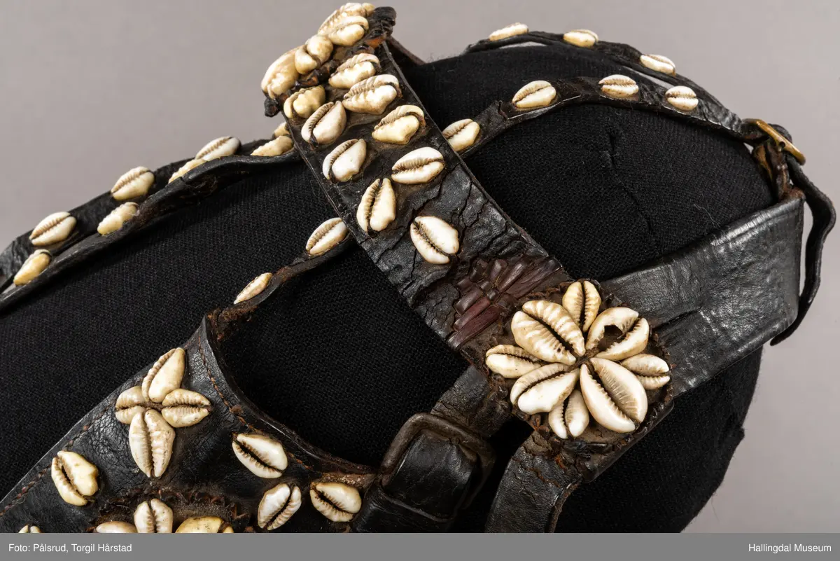 Hodelag til hest med munnbitt og tømmer. Hodelaget er dekoret med kauriskjell og rød ull. Skylapper, trapesformet dekorert midt på med lærrosett og hvite kauriskjell. Kort tømme, ender i kute av lærfletting og røde ullfrynser, frynsene er slitt bort. Munnbitt av jern. Stassele.