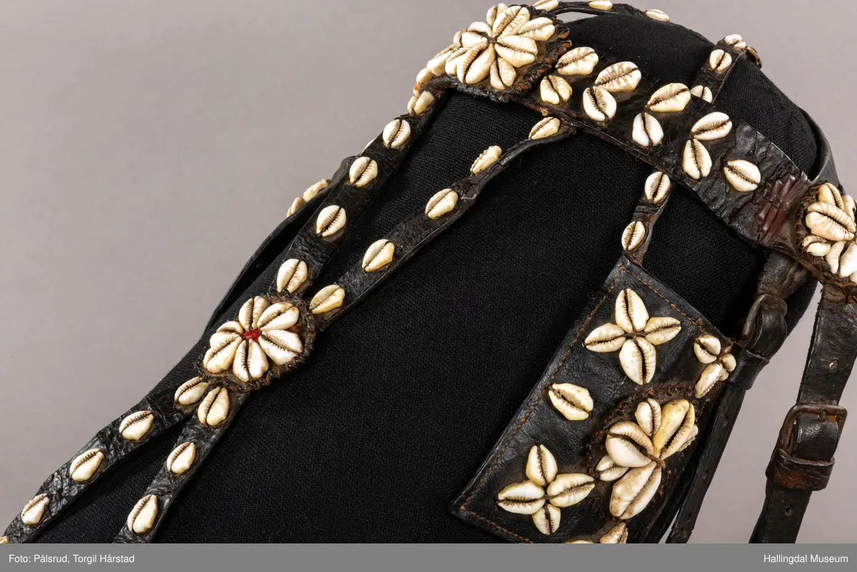 Hodelag til hest med munnbitt og tømmer. Hodelaget er dekoret med kauriskjell og rød ull. Skylapper, trapesformet dekorert midt på med lærrosett og hvite kauriskjell. Kort tømme, ender i kute av lærfletting og røde ullfrynser, frynsene er slitt bort. Munnbitt av jern. Stassele.