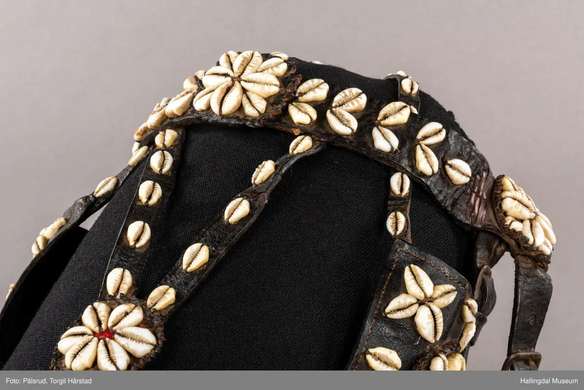 Hodelag til hest med munnbitt og tømmer. Hodelaget er dekoret med kauriskjell og rød ull. Skylapper, trapesformet dekorert midt på med lærrosett og hvite kauriskjell. Kort tømme, ender i kute av lærfletting og røde ullfrynser, frynsene er slitt bort. Munnbitt av jern. Stassele.