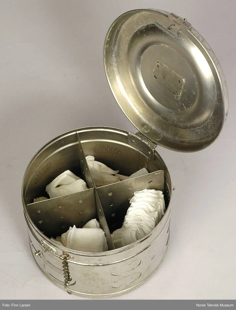 Rund metallbeholder med lokk og fire kamre inni. Beholderen / kolben har ventileres. Inne i beholderen er det kompresser. Man ville sterilisere disse ved å dynke noen dråpe formalin over, tette beholderen, sette den i et steriliseringsskap og så ventilere kompressene. Dette var en metode som ble brukt fram til begynnelsen av 1970-tallet da steriliseringsskap kom som kunne brukes uten formalin. Det hørte til sykepleiernes arbeid å sterilisere og brette kompressene, og mange husker formalinlukten som ille.