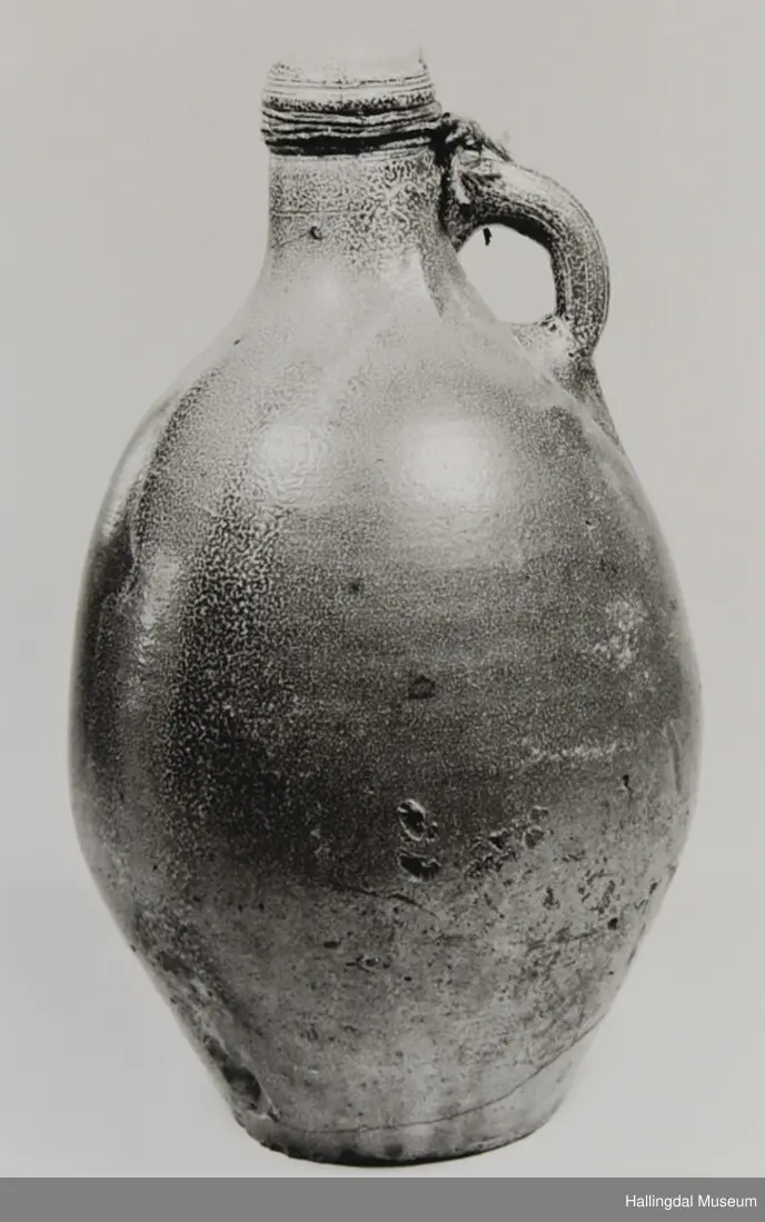 Sirkulært tverrsnitt, kvelva sider, skrår fyrst utover og deretter kraftig innover mot halsopning. Hank øvst ved halsen.