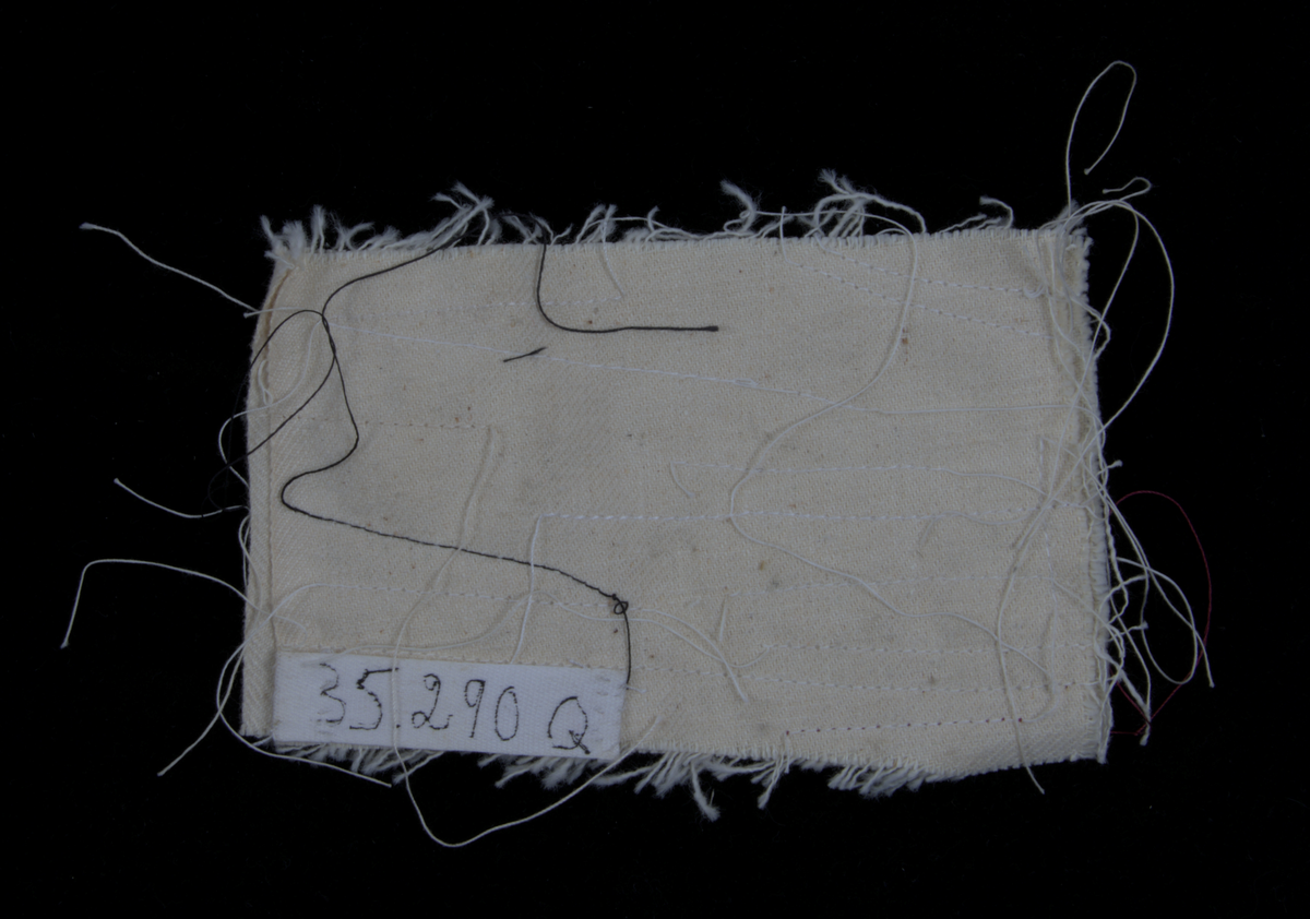 a) Symaskin av märket Husqvarna, modell V.S.4. Handdriven. Svartmålad på träplatta. Nersänkt låda med tillbehör. b) Huv av ekfaner. Handtag på toppen. c) Skyttel av stål. Rund, spetsig i ena änden, rak i den andra. Innehåller en spole med vit tråd. d) Fem spolar av stål. Rund stav med plattor i ändarna. Olika trådrester. e) Ledpressarfot (monterad på maskinen). f) Fållvikare 2 mm. g) Fållvikare 6 mm. h) Gansapparat. i) Rynkfot .j) Linjal. Längd 5,3 cm. k) Fem symaskinsnålar i olika grovlekar. Cellofanförpackning. l) Skruvnyckel. Typ lång platt nål, bakre delen försedd med runt hål. m) Skruvmejsel av stål. Fäste av svart bakelit. n) Borste av dubbelvriden ståltråd med en borste i ena änden. o) Skruvmejsel av stål. Fäste av svart bakelit. p) Provlapp av bomullsflanell. För kontroll av stygnställning. q) Provlapp av bomyllskypert. Till kontroll av stygnställning. r) Bruksanvisning. Tryckt broschyr på 30 sidor.