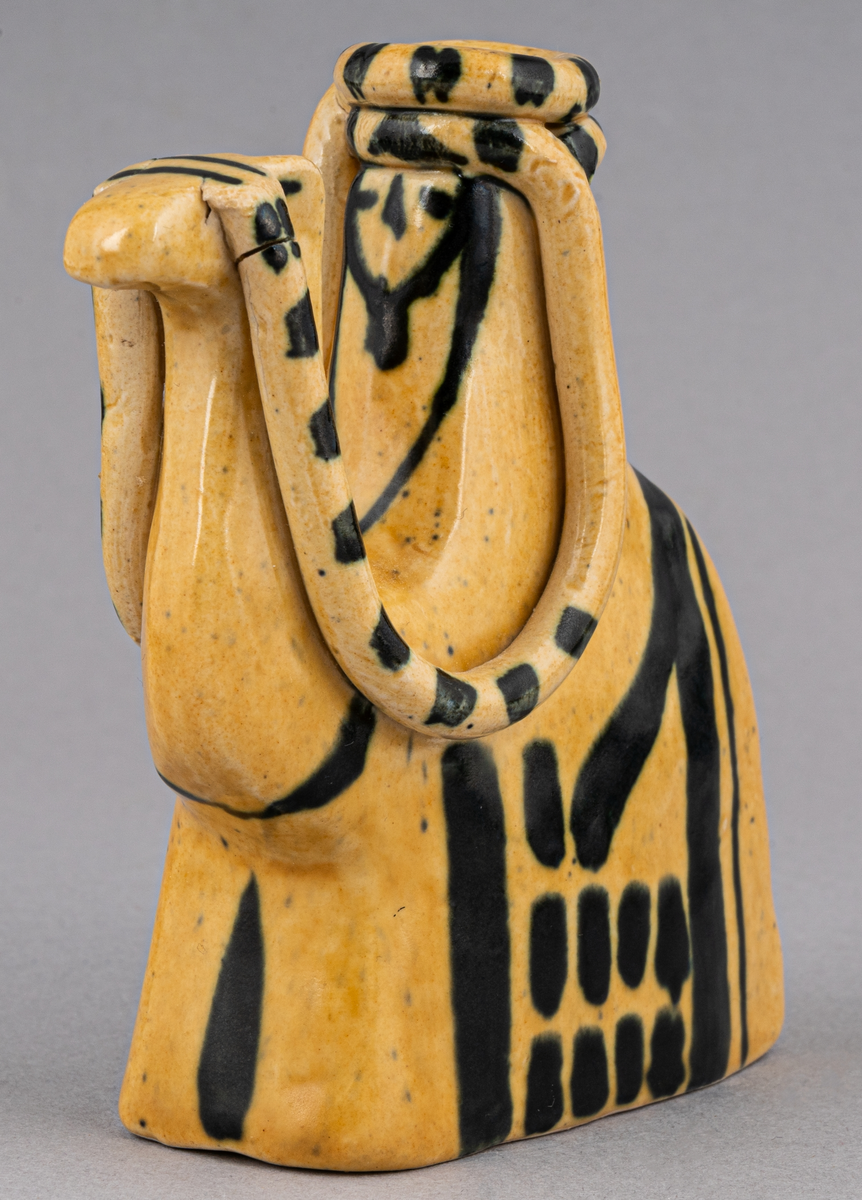 Figurin i lergods, kan även användas som ljusstake för julgransljus. Modell 6001, formgiven av Eva Jancke Björk under 1940- eller 1950-talet. Glasyr/dekor SV; curryfärgad bottenglasyr med svart dekor. Figurinen föreställer en arab sittandes på en kamel.