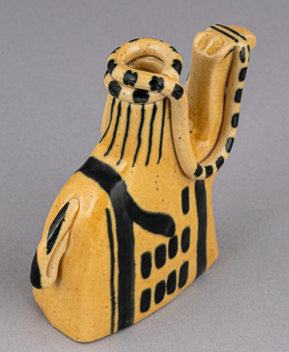 Figurin i lergods, kan även användas som ljusstake för julgransljus. Modell 6001, formgiven av Eva Jancke Björk under 1940- eller 1950-talet. Glasyr/dekor SV; curryfärgad bottenglasyr med svart dekor. Figurinen föreställer en arab sittandes på en kamel.