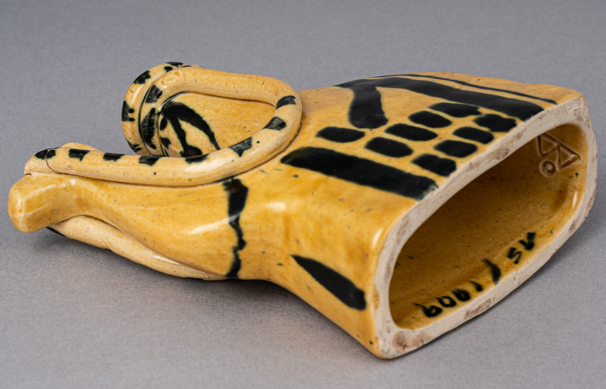 Figurin i lergods, kan även användas som ljusstake för julgransljus. Modell 6001, formgiven av Eva Jancke Björk under 1940- eller 1950-talet. Glasyr/dekor SV; curryfärgad bottenglasyr med svart dekor. Figurinen föreställer en arab sittandes på en kamel.