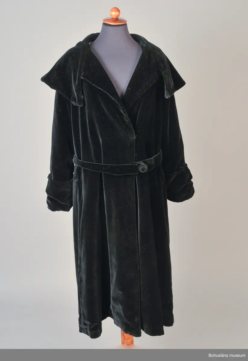 Kappa i svart sammet med vitt sidenfoder. Pellerinkrage och löst sittande skärp.