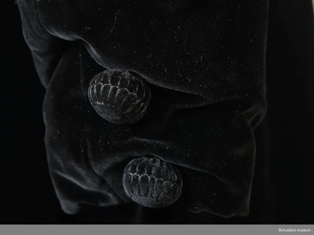 Kappa i svart sammet med vitt sidenfoder. Pellerinkrage och löst sittande skärp.