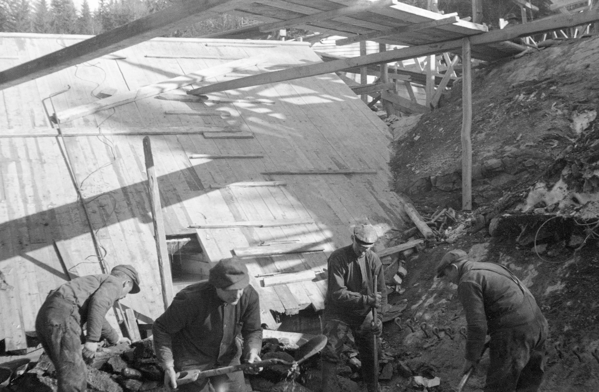 Fra bygginga av en ny dam ved Sølvstufossen, øverst i Ågårdselva i Tune i Østfold, som er en del av Nedre Glommas vestre løp. Anleggsarbeidet startet vinteren 1936, i en periode da det knapt rant vann i elveløpet. Dette fotografiet er tatt noe seinere, etter at snøen i terrenget hadde smeltet bort, og etter at mye av murverket var ferdigstilt. Fotografiet viser fire menn i arbeid med spett og spader i elveleiet foran et skråplan av tre, antakelig et damløp, med en kvadratisk åpning nederst, antakelig til bunnluka. Over dem et stillas med kjøregang av tre. På forskalinga var det påspikret en del tverrstilte bord, antakelig for å gjøre det mindre farefullt å gå opp og ned fra elveleiet. Ågårdselva er et cirka fem og en halv kilometer langt vassdrag som renner fra den nordvestre enden av Isnesfjorden (Vestvannet) i Nedre Glommas vestre løp, sørvestover gjennem berglendt terreng mot innsjøen Visterflo. Høydeforskjellen mellom Isnesfjorden og Visterflo er på bortimot 25 meter. Ågårdselva har tre fossefall, det øverste her ved Sølvstu, deretter ved Valbrekke og nederst ved Solli. Behovet for den dambygginga vi ser på dette fotografiet var forårsaket av selskapene Borregaards og Hafslunds inngrep i Glommas østre løp, hovedløpet, som i lavvannsperioder gjorde det svært vanskelig å få tømmer som skulle til bedrifter nedenfor Sarpsfossen via Mingevannet, Isnesfjorden og tømmertunnelen til Eidet gjennom det trange sundet ved Trøsken. Dette forsøkte man å løse ved å heve vannspeilet i Isnesfjorden med en dam som skulle plasseres 10-15 meter ovenfor den eksisterende dammen ved Sølvstufossen. Se mer informasjon under fanen «Opplysninger».